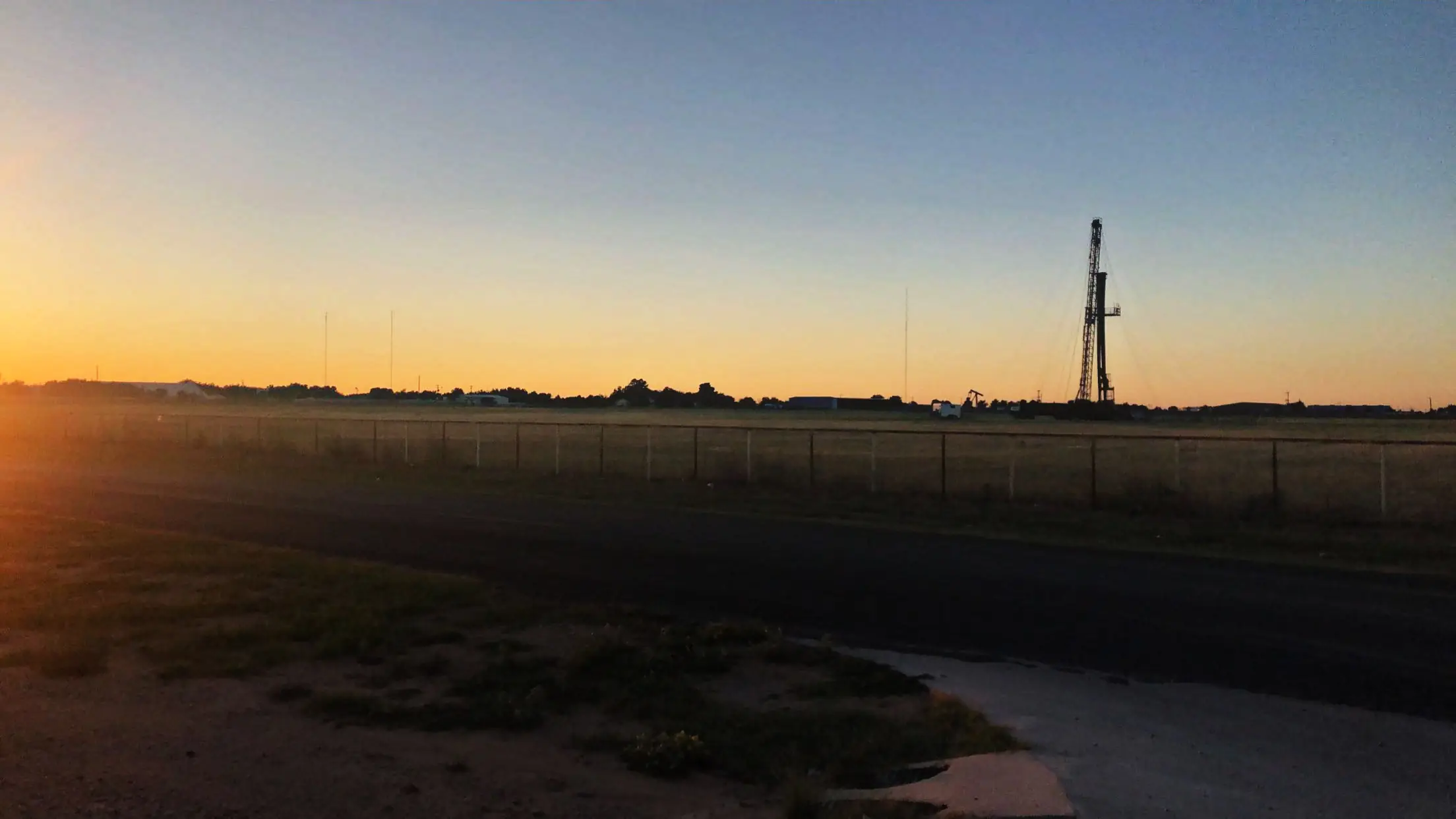 A drilling rig on the horizon of flat Texas country at sunset.